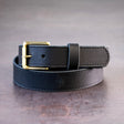 Black belt with brown stitching and brass hardware sitting on metal surface