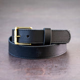 Black belt with brown stitching and brass hardware sitting on metal surface