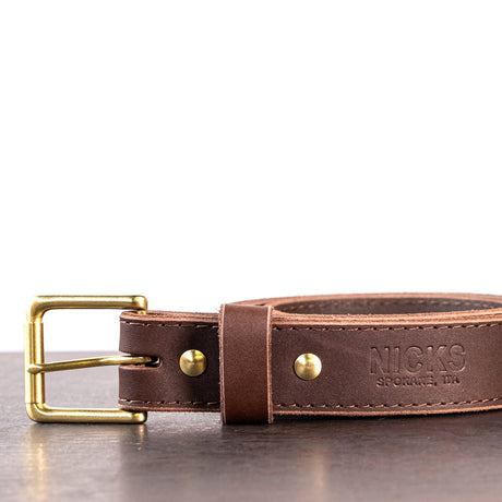 Dark brown belt with brown stitching and brass hardware sitting on metal surface
