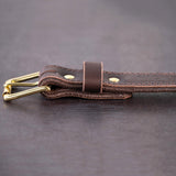Dark brown belt with brown stitching and brass hardware sitting on metal surface