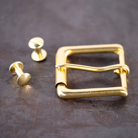 Brass belt buckle and brass Chicago screws sitting on a metal surface