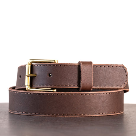 Dark brown belt with brown stitching and brass hardware sitting on metal surface with white background