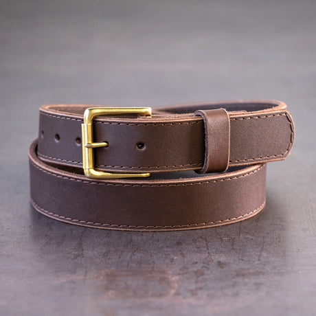 Dark brown belt with brown stitching and brass hardware sitting on metal surface
