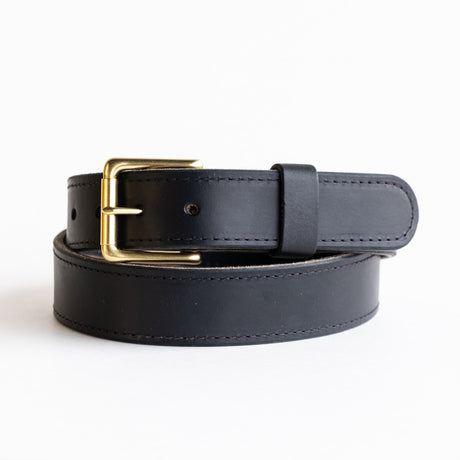 Close-up of a black leather belt with a smooth finish, featuring a simple brass buckle and visible grain details, showcasing its timeless and rustic craftsmanship.