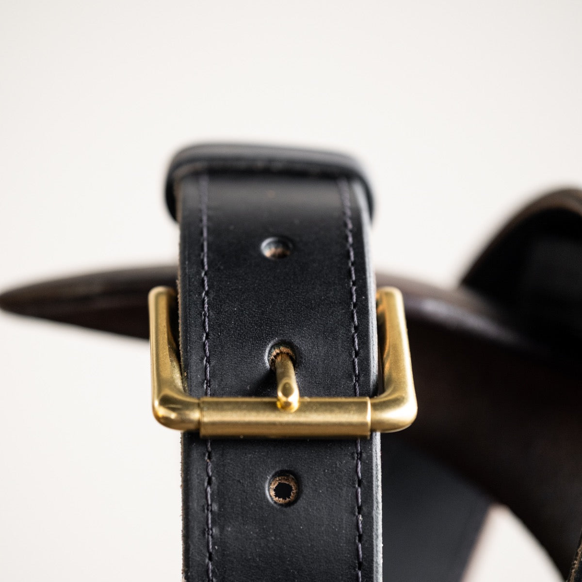Close-up of a black leather belt with a smooth finish, featuring a simple brass buckle and visible grain details, showcasing its timeless and rustic craftsmanship.
