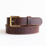 Close-up of a brown leather belt with a smooth finish, featuring a simple brass buckle and visible grain details, showcasing its timeless and rustic craftsmanship.