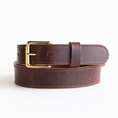 Close-up of a brown leather belt with a smooth finish, featuring a simple brass buckle and visible grain details, showcasing its timeless and rustic craftsmanship.