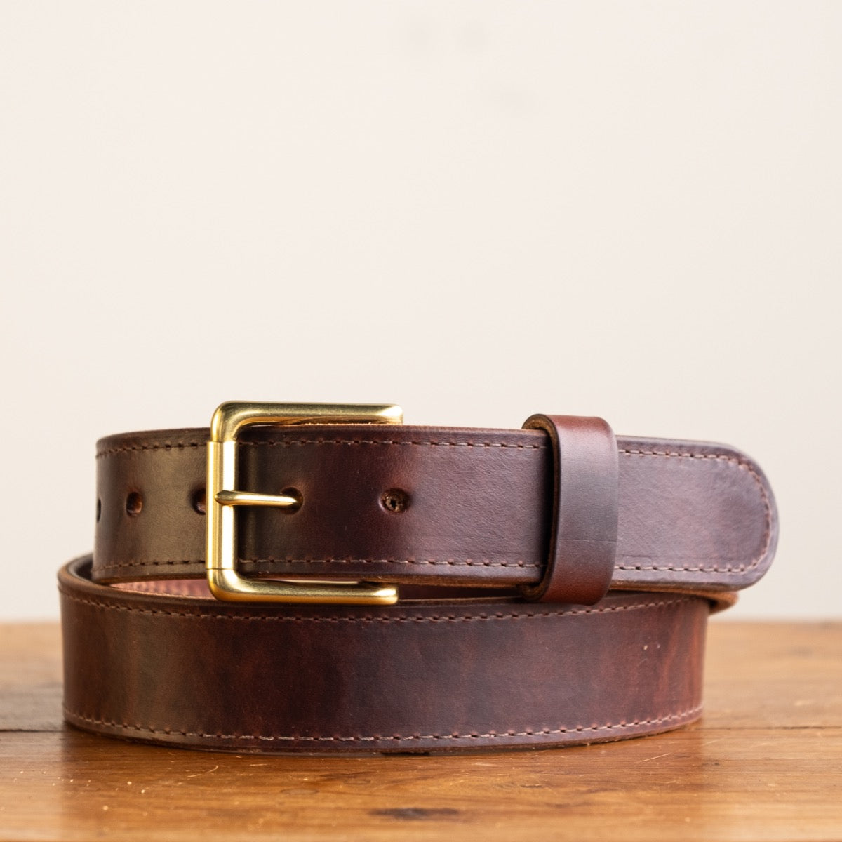 Close-up of a brown leather belt with a smooth finish, featuring a simple brass buckle and visible grain details, showcasing its timeless and rustic craftsmanship.