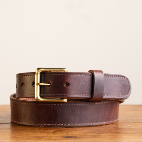 Close-up of a brown leather belt with a smooth finish, featuring a simple brass buckle and visible grain details, showcasing its timeless and rustic craftsmanship.