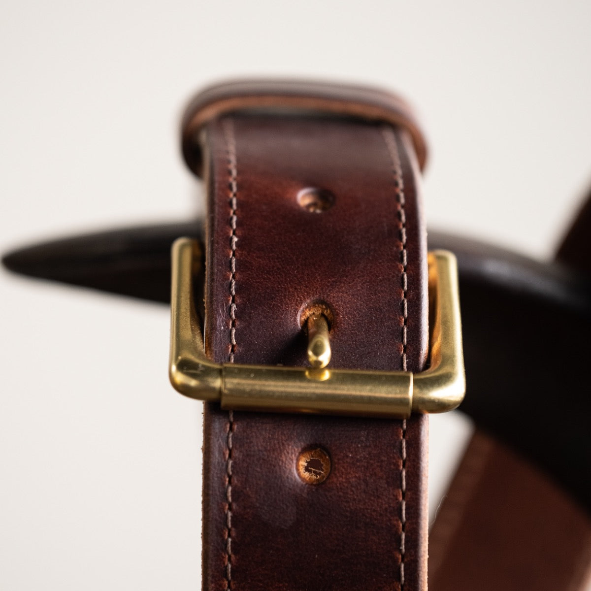 Close-up of a brown leather belt with a smooth finish, featuring a simple brass buckle and visible grain details, showcasing its timeless and rustic craftsmanship.