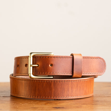 Close-up of a natural leather belt with a smooth finish, featuring a simple brass buckle and visible grain details, showcasing its timeless and rustic craftsmanship.