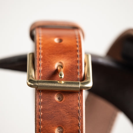 Close-up of a natural leather belt with a smooth finish, featuring a simple brass buckle and visible grain details, showcasing its timeless and rustic craftsmanship.