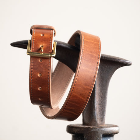 Close-up of a natural leather belt with a smooth finish, featuring a simple brass buckle and visible grain details, showcasing its timeless and rustic craftsmanship.